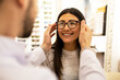 © ADDICTIVE STOCK - Happy woman trying on different eyeglass frames in store