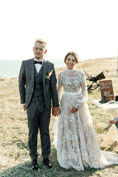 bride and grooms sit at the wedding ceremony surrounded by rustic decorations and wildflowers. wedding ceremony outside the city with a sea view