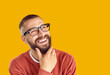 © Studio Romantic - Joyful dreamy man imagining or thinking about something pleasant isolated on orange background. Close up of positive caucasian bearded man wearing glasses holding chin looking at copy space.
