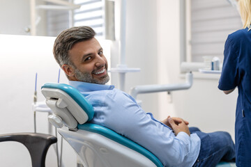 Wall Mural - Image of satisfied man sitting in dental chair at medical center while professional doctor fixing his teeth