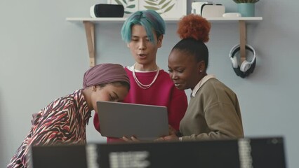 Blue haired Asian guy with laptop and his two diverse female colleagues discussing software development, working together in contemporary office