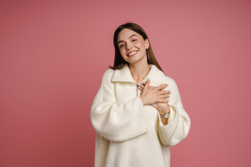 Wall Mural - Smiling woman holding hands on her chest isolated over pink background