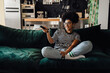 © Drobot Dean - Cheerful african woman watching TV while sitting on couch