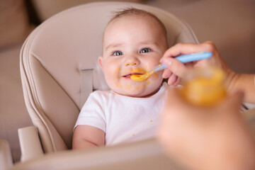 Cute baby boy being fed with porridge by his mother