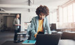 © Flamingo Images - Young businesswoman working on a laptop with colleagues talking in the background