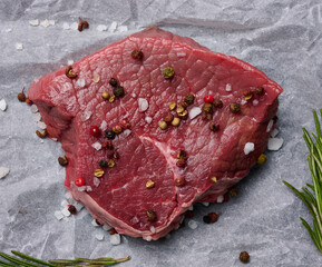 Wall Mural - Raw piece of beef with spices lies on a white piece of parchment paper, top view