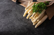 Fresh white asparagus on black background. Seasonal spring vegetables on black stone slab. Sunny kitchen still life for healthy  nutrion. Gastronomy background with space for text.