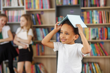 Wall Mural - Back to school. Mixed-race schoolboy with book on head having fun.