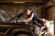 © Austockphoto - Female mechanic sitting on car hood leaning in repairing the car in workshop
