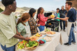 Multi generational people doing barbecue at home's rooftop - Multiracial friends having fun eating and cooking together during weekend day - Summer and food concept - Main focus on african woman face