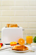 Healthy breakfast in the kitchen. Toaster and bread toast, freshly squeezed orange juice. Cheese, butter, lettuce. White toaster with healthy food and drinks on table in light kitchen
