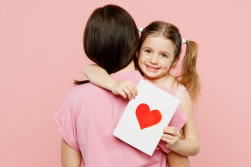 Wall Mural - Back rear view woman wear casual clothes with child kid girl 6-7 years old. Daughter give mother postcard with heart, hug and cuddle isolated on plain pastel pink background Family parent day concept