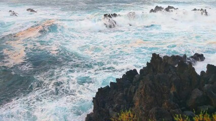 Wall Mural - Beautiful blue waves crash against the rocks on the shore of the sea or ocean