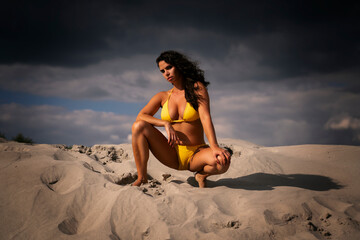 Dominant serious strong woman posing on cloudy day, dark sky in swimsuit