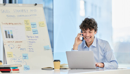 Poster - This is shaping up to look amazing. a young businessman making a phone call on his smartphone while working on a laptop.