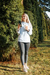 © Sergio - Smiling slim young blonde woman using smartphone in park, lifestyle. Cheerful caucasian female student holding phone and looking away on sunny day outdoors