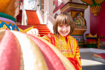 Wall Mural -  a happy boy in a Russian national bright red-orange costume near the Russian national multi-colored Terem building.