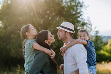 Wall Mural - Portrait of young couple with their daughters in the nature, kissing. Side view.