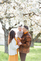 Happy young family with little son walks in blooming garden. Mom and dad with 1 year old baby. Spring.