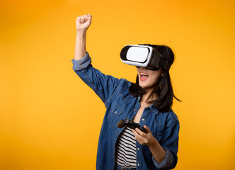 Poster - Young asian woman happy success wearing virtual reality headset game entertainment and holding joystick controller isolated on yellow background. Winner of cyber future video game concept.