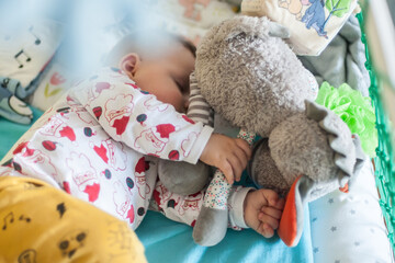 Wall Mural - A cute little baby boy is sleeping peacefully and relaxed on his bed with toys. Top view of the crib. Love and family emotions