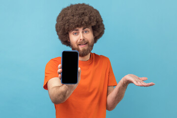 Wall Mural - portrait of confused man with afro hairstyle wearing orange t-shirt showing cell phone with blank bl