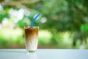 Iced coffee on white table, green background. Cold beverage in summer.