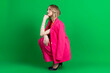 © Georgi - Young curly blonde dressed in pink blazer and pants, crouches and thoughtfully looking up. Isolated on green background.