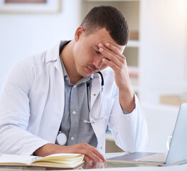 Poster - I couldnt have gotten worse news. a handsome young doctor sitting alone in his clinic and feeling stressed while using his laptop.