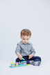 © DSMT - A little boy in a shirt is building a colorful wooden toy on a white background. The concept of children's development, games for children, toys. Copy space