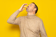 Bearded Hispanic man wearing a beige turtleneck smacking his lips and licking his fingers after devouring an exquisite delicacy, isolated on yellow studio background.