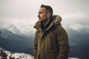 Wall Mural - Handsome young man in warm jacket standing on top of mountain and looking away