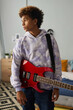 © Seventyfour - Serene teenage guy with electric guitar hanging on his shoulder standing in front of camera in home environment and looking aside