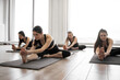 Young healthy females in sportswear doing Janu Sirsasana exercise on black mats in meditation room. Athletic caucasian yoginis eliminating mild depression while taking up Head to Knee Pose indoors.