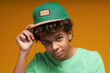 © Seventyfour - Calm teenage boy in t-shirt touching visor of green baseball cap and looking at camera while posing during photo session in isolation