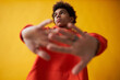 © Seventyfour - Cute African American teenage boy in red hoodie stretching arms in front of himself while posing on yellow background during photo session