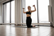 © sofiko14 - Front view of sporty young lady standing on knees on yoga mat and training arms with dumbbells. Caucasian fitness woman dressed in comfy active clothes performs sports exercises in studio.