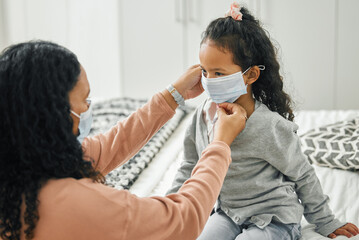 Wall Mural - We can never forget our masks. a young mother and daughter putting on masks at home.