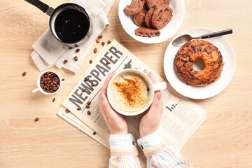 Wall Mural - Woman with cup of coffee, newspaper and pastry on light wooden background