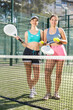 © JackF - Sportive young women tennis players posing by the net holding Padel racket and ball in open-air court