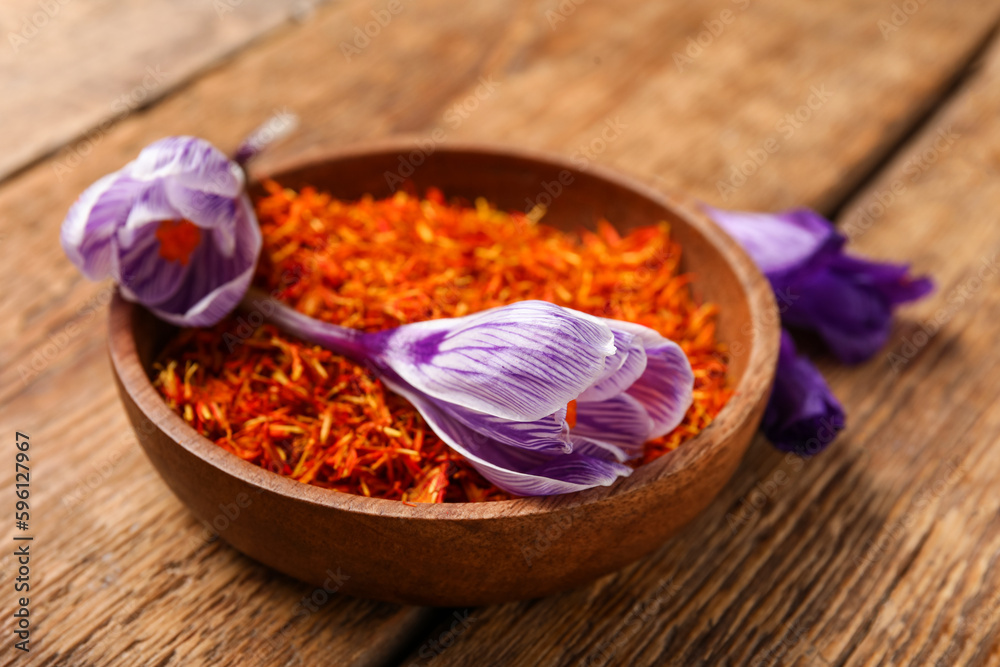 Bowl of dried saffron threads with crocus flowers on wooden table