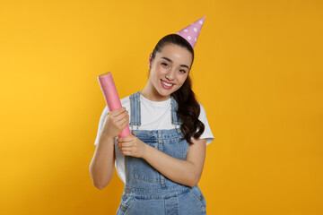 Poster - Young woman blowing up party popper on yellow background