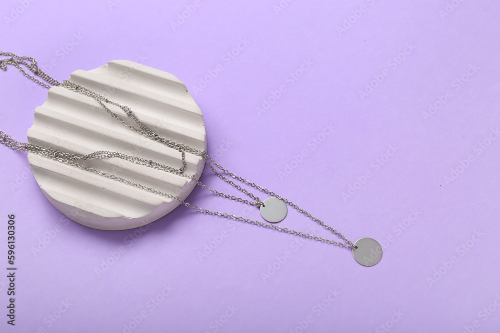 Showcase pedestal with silver necklaces on lilac background