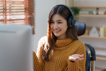 Asian woman having video call on her computer at home. listening to online lecture, taking notes, online study at home