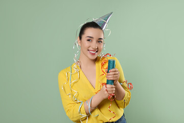 Poster - Young woman blowing up party popper on pale green background