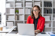 © amnaj - Charming businesswoman sitting working on laptop computer in office.