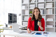 © amnaj - Happy young businesswoman sitting working holding coffee and take notes at office.