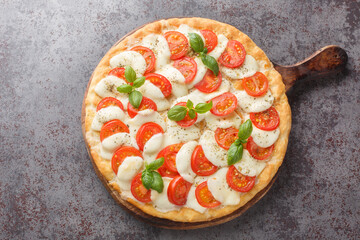 Canvas Print - Caprese pizza with melted mozzarella, tomatoes and basil leaves close-up on a wooden board on the table. horizontal top view from above