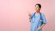 © bongkarn - A doctor with stethoscope pointing aside while standing on the pink isolate background.