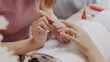 Close up Asian nail stylist apply color for a perfect polish nail to customer. Manicure concept. Nail salon services.